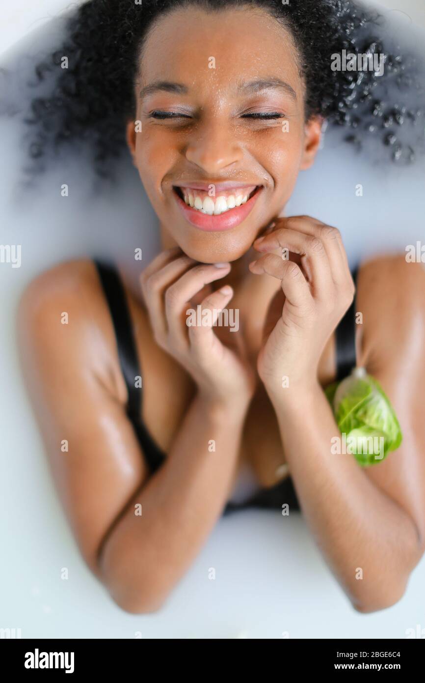 Portrait of happy black girl taking milk bath and wearing bra Stock