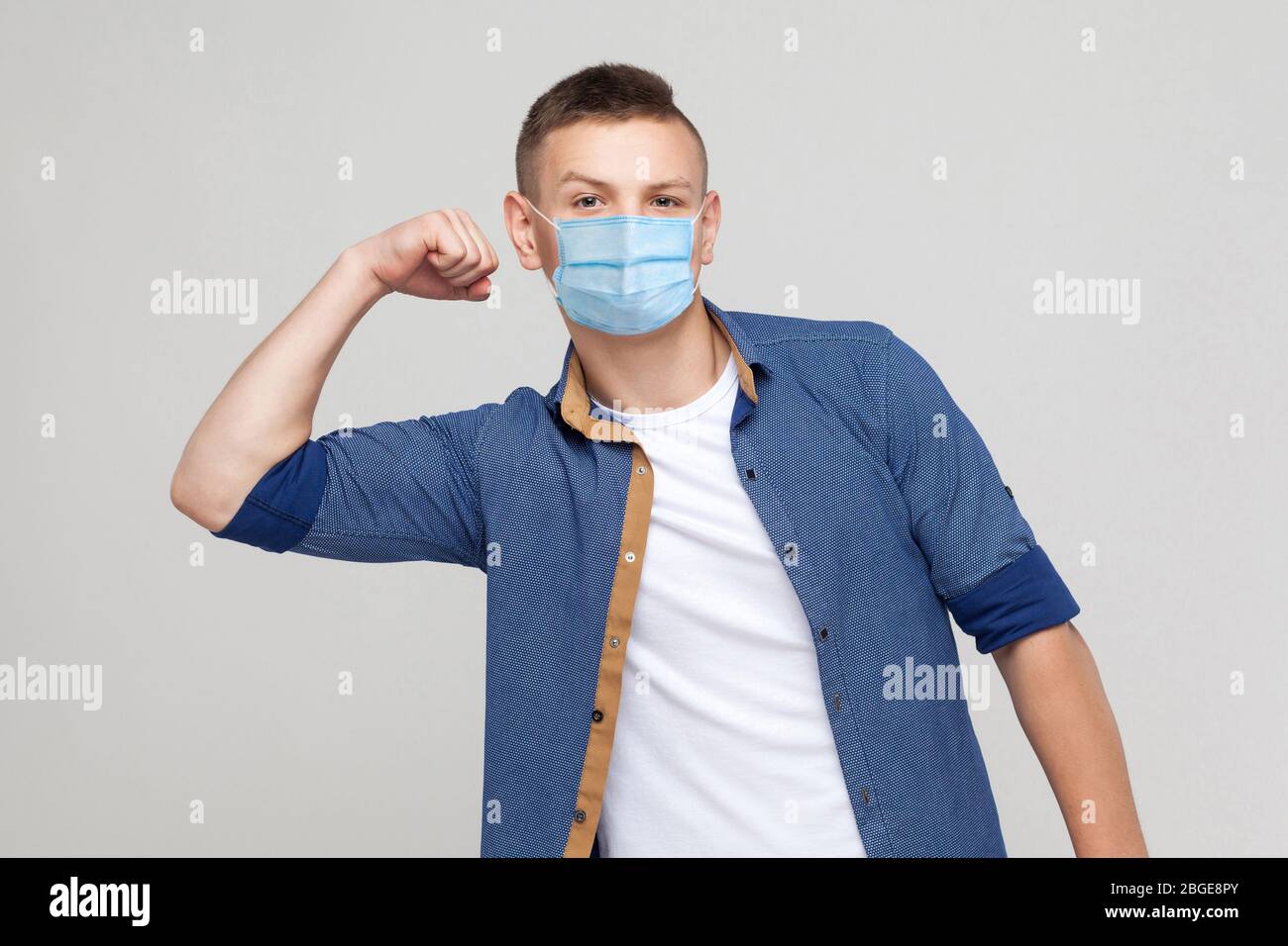 I am strong. Portrait of haughty young man in casual style with surgical medical mask standing with raised arms and looking at camera with proud face. Stock Photo