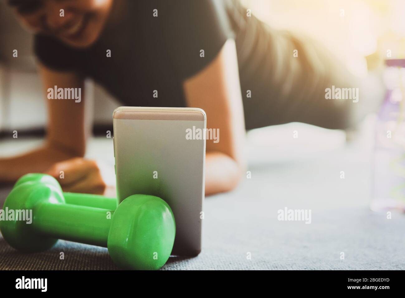 A sporty woman using smartphone during workout at home in the living room. Online personal trainer or on mobile phone.Sport and recreation concept.adv Stock Photo