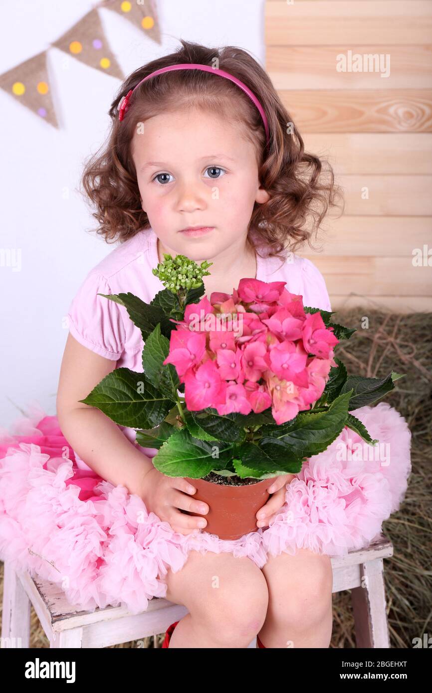 Beautiful small girl in petty skirt holding flowers on country style background Stock Photo