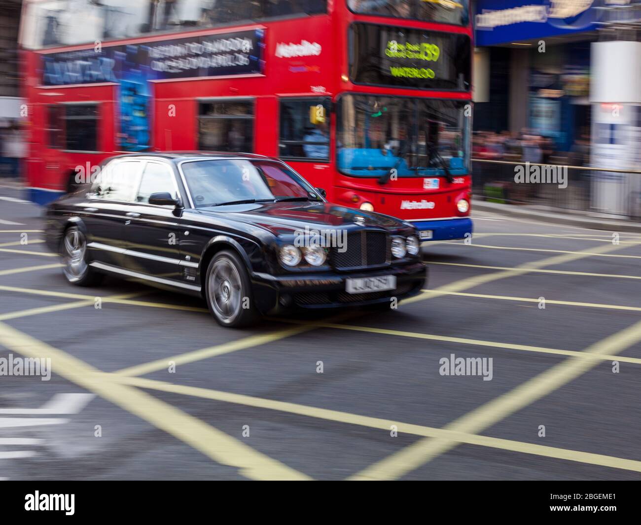 Rolls Royce car and Red London Bus cross Piccadilly Circus in Central London's West End District. Wealthy London / London Wealth. Motion Blur. Stock Photo