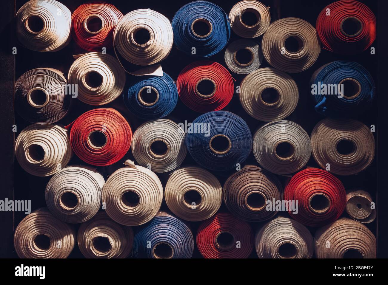 many textile rolls of blue, white and orange colors stacked one over the other in dark light Stock Photo