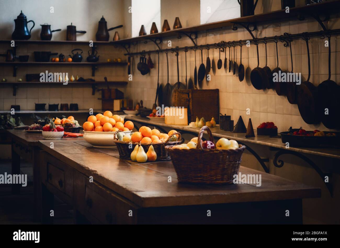 antique XIX century old kitchen with tools, pans, pots and food ingredients all over che benches and tables Stock Photo