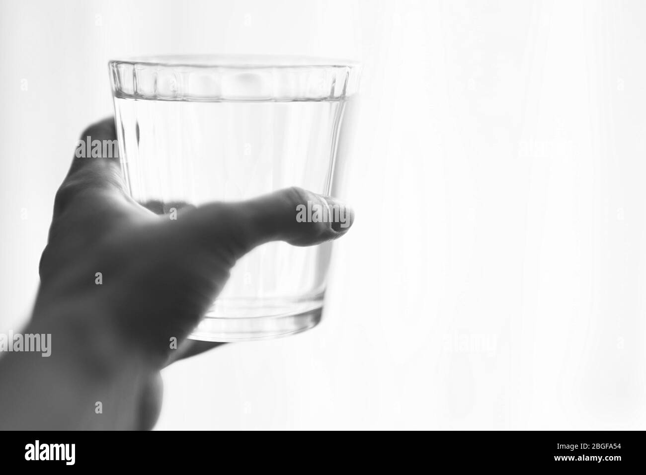 Full glass of water in a female hand on a white background, place for text, bw photo. Stock Photo