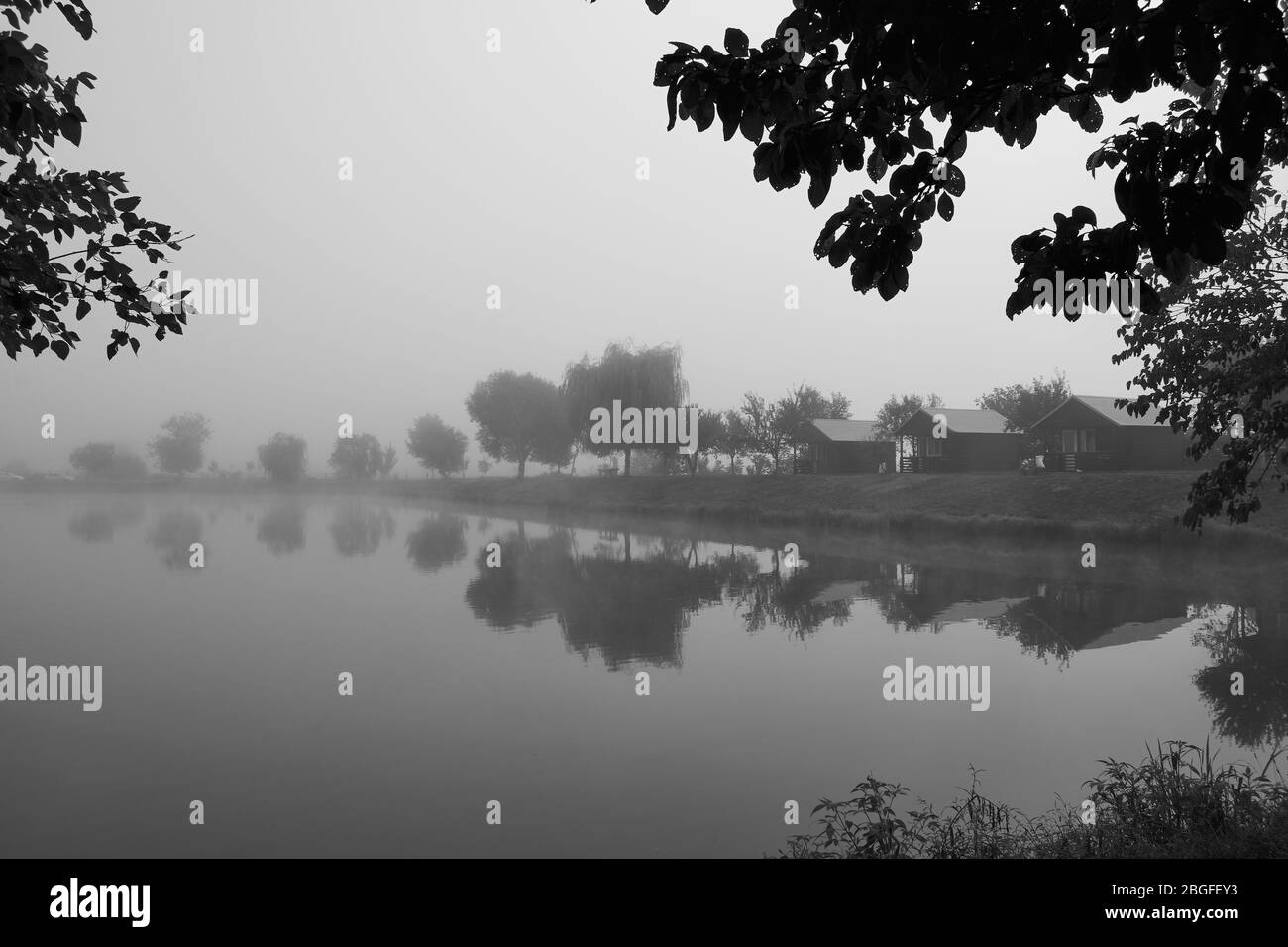 landscape with lake, trees and blue sky with clouds covered in mist Stock Photo