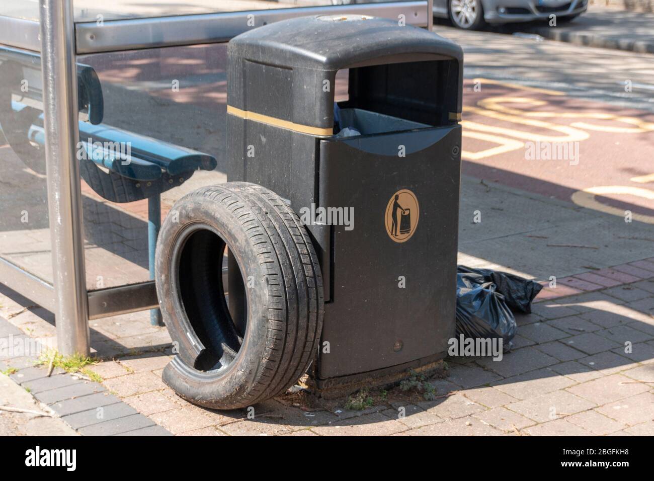 a close up view of a car tyre and black bags that have been left next to a public rubbish bin Stock Photo