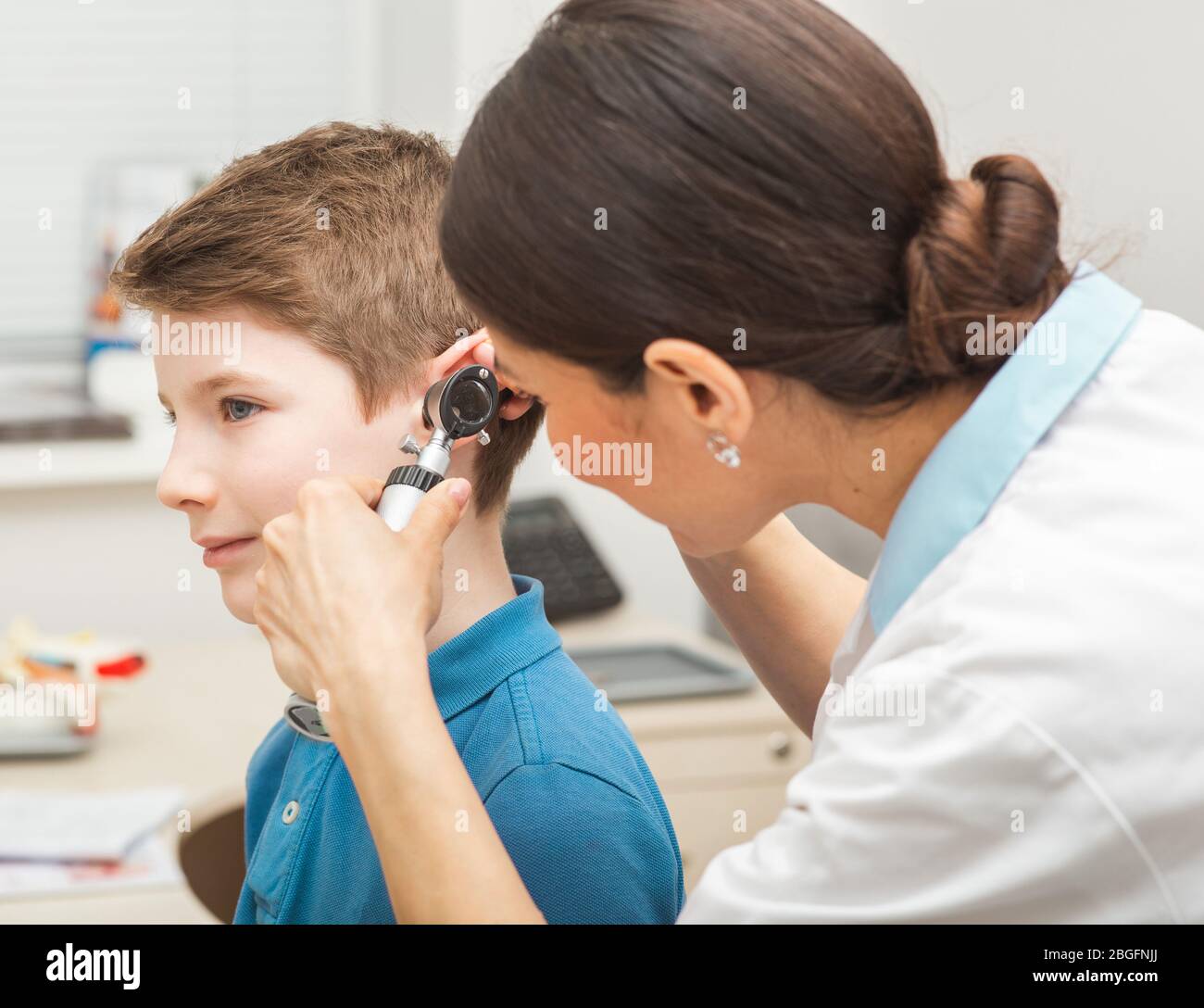 Audiologist examining boy ear , using otoscope, in doctors office