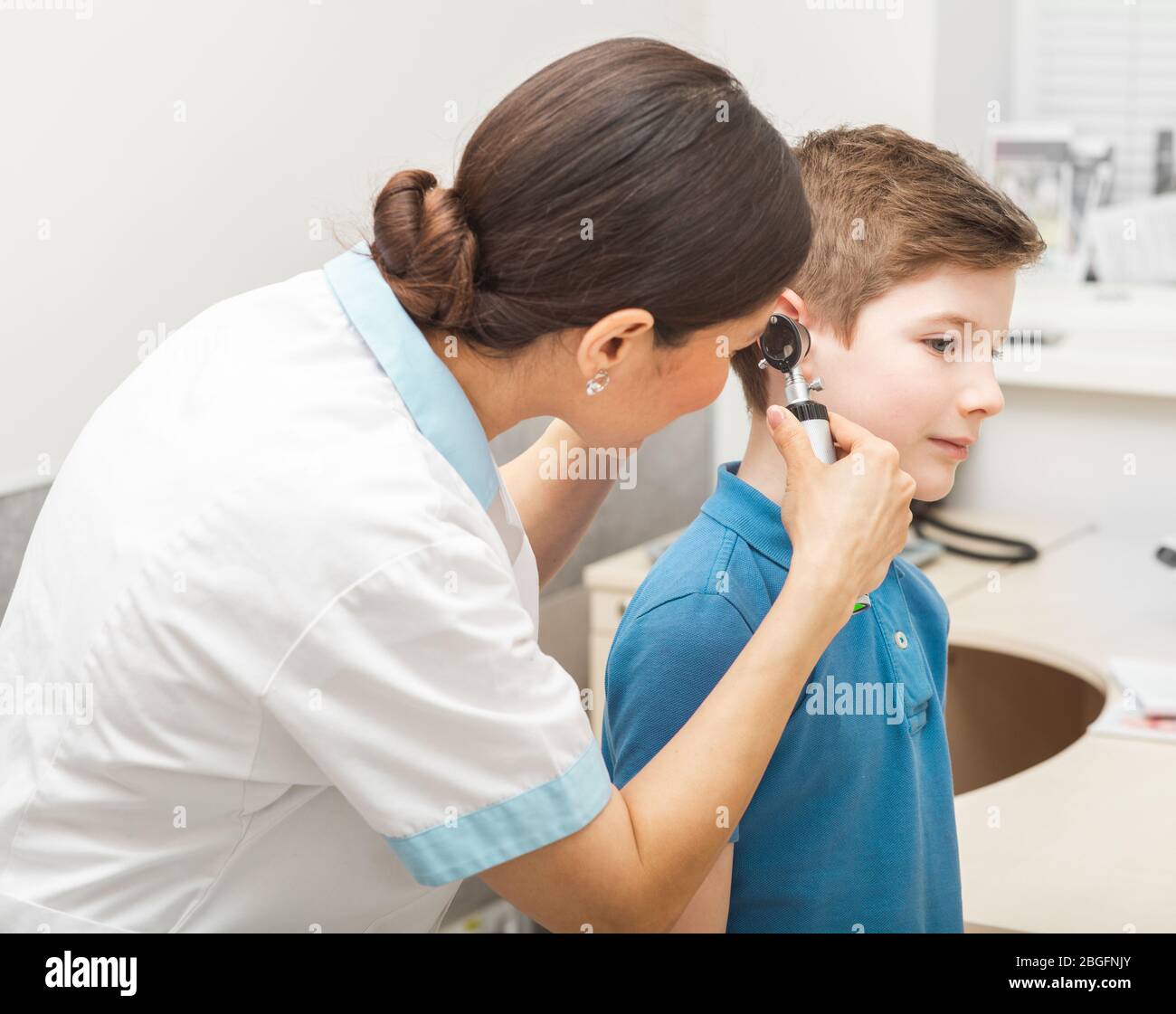 Audiologist examining boy ear , using otoscope, in doctors office. Child receiving a hearing