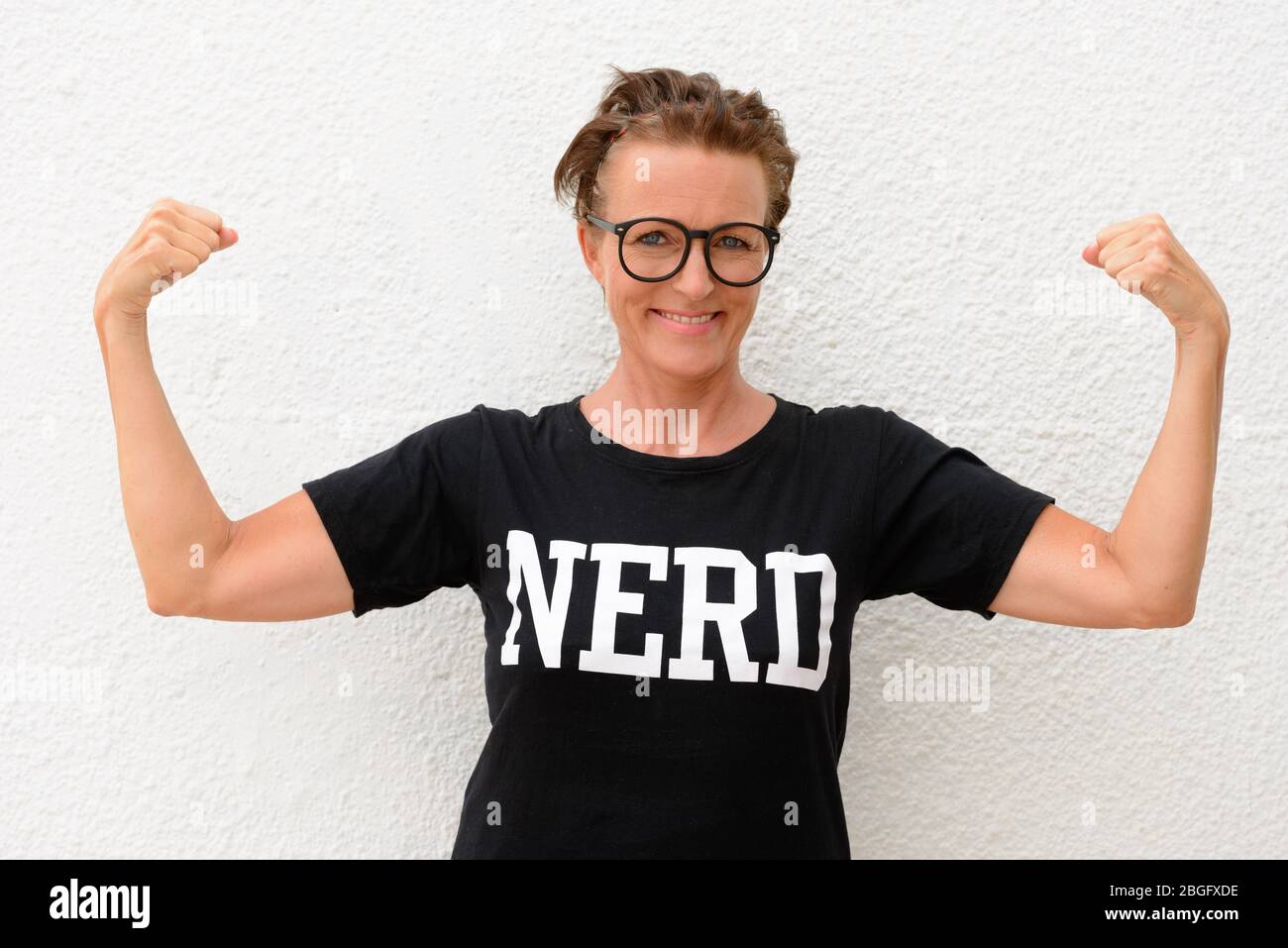 Happy mature nerd woman wearing big eyeglasses and flexing muscles while standing against white background outdoors Stock Photo