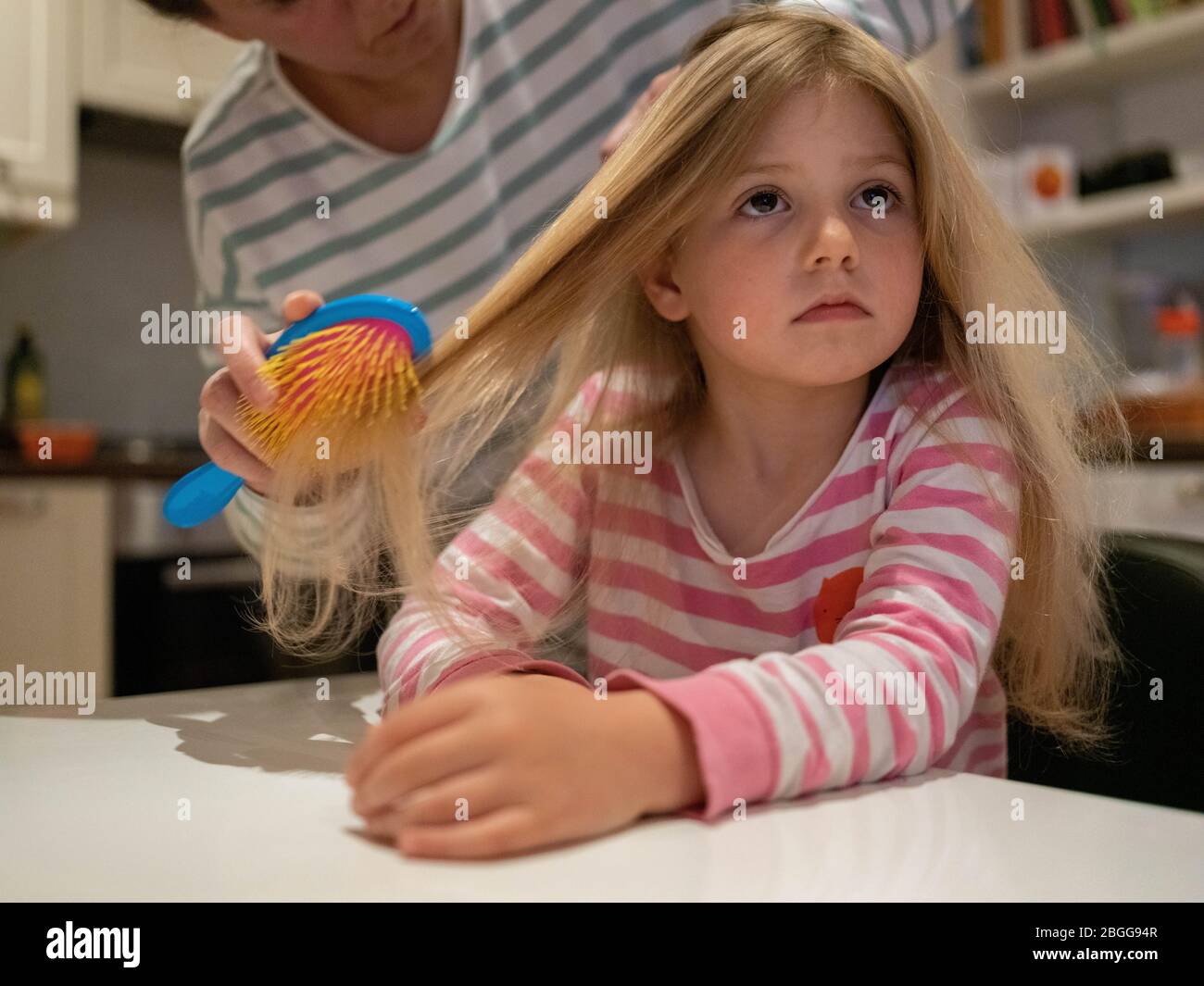 A four year old girl with long blond hair is having her hair brushed by
