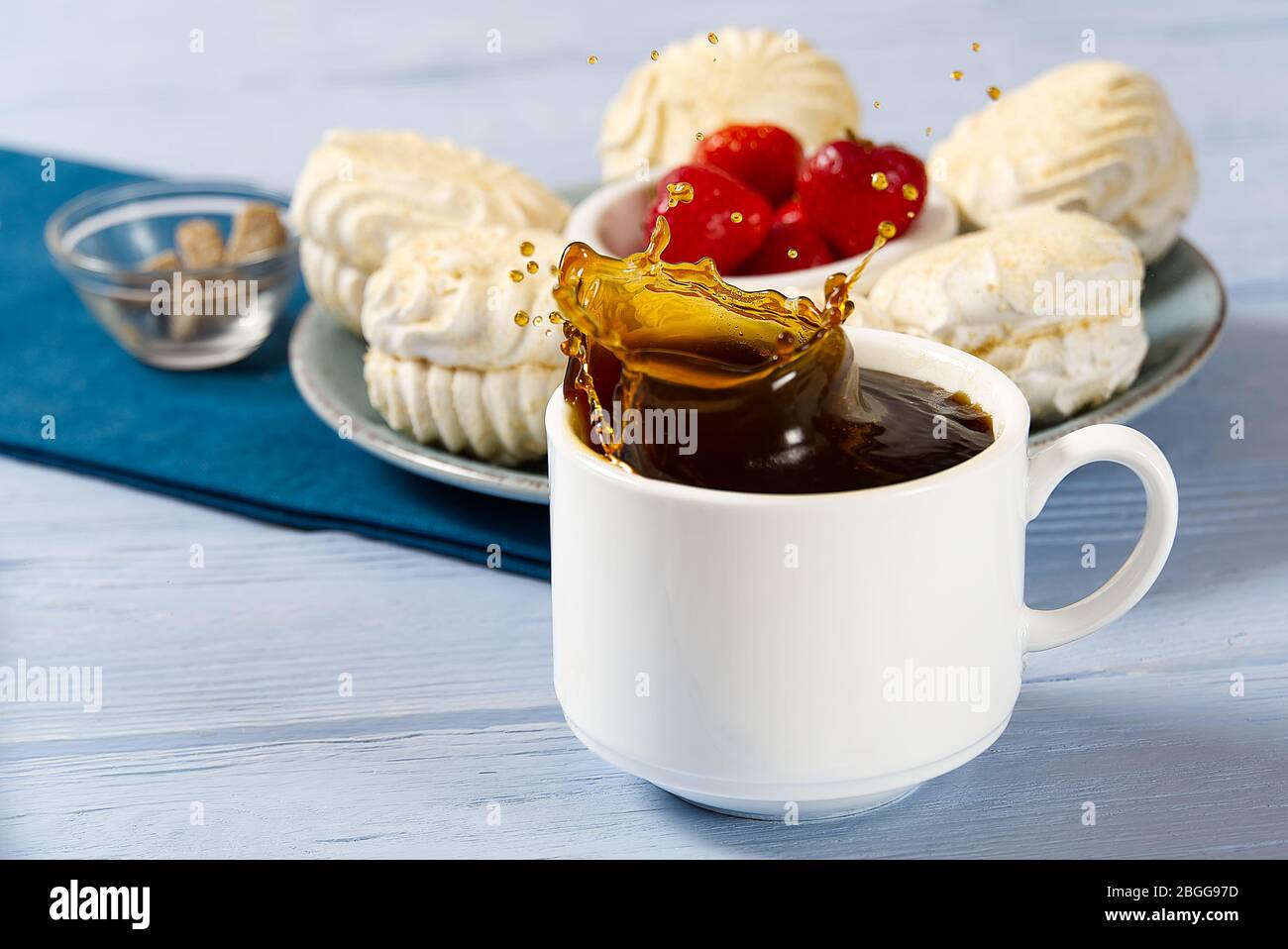 Drop falling into a cup of coffee. On a light blue wooden background ...