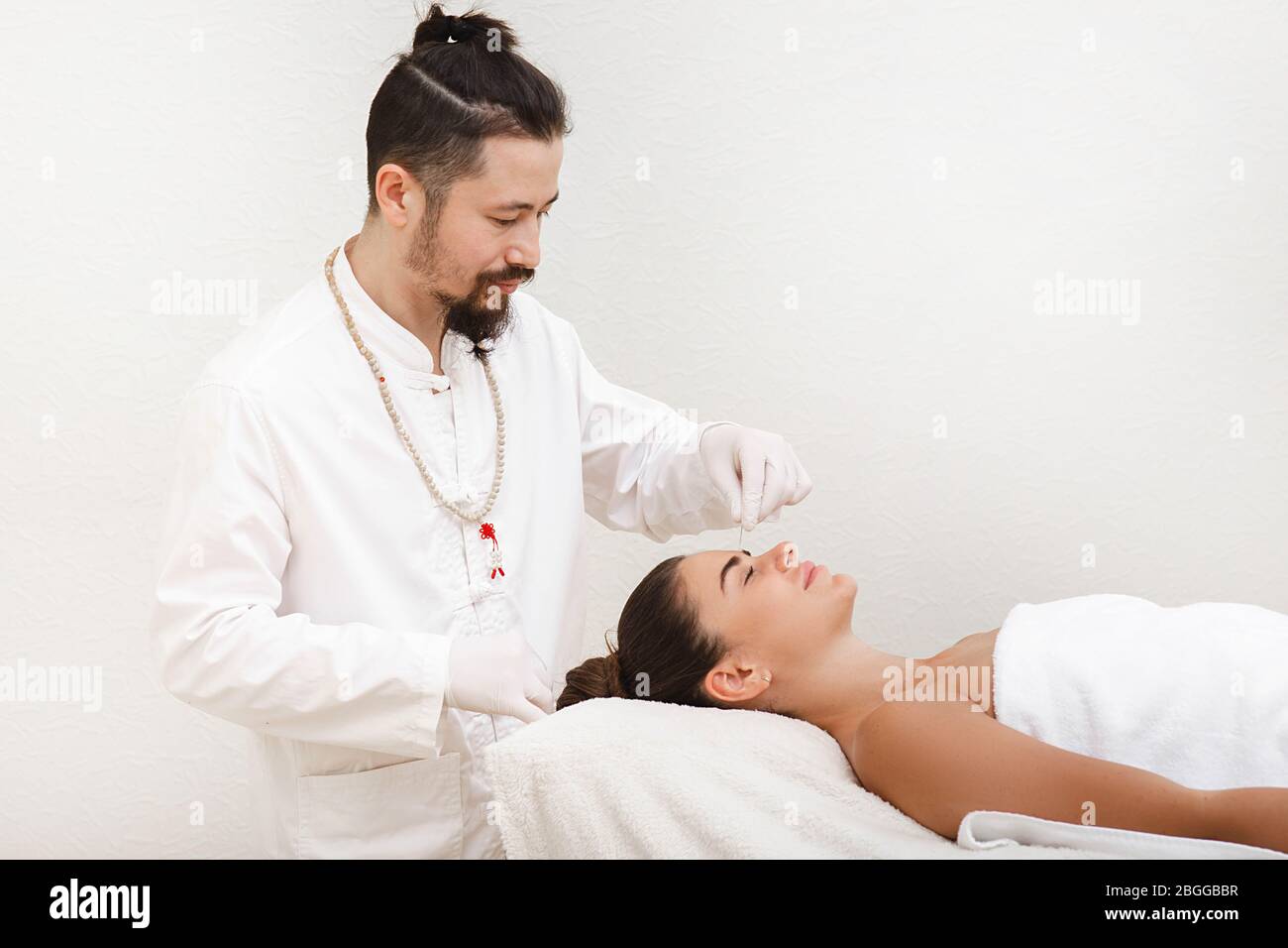 Traditional Chinese medicine doctor doing acupuncture on woman's forehead to relieve stress and migraine. Stock Photo