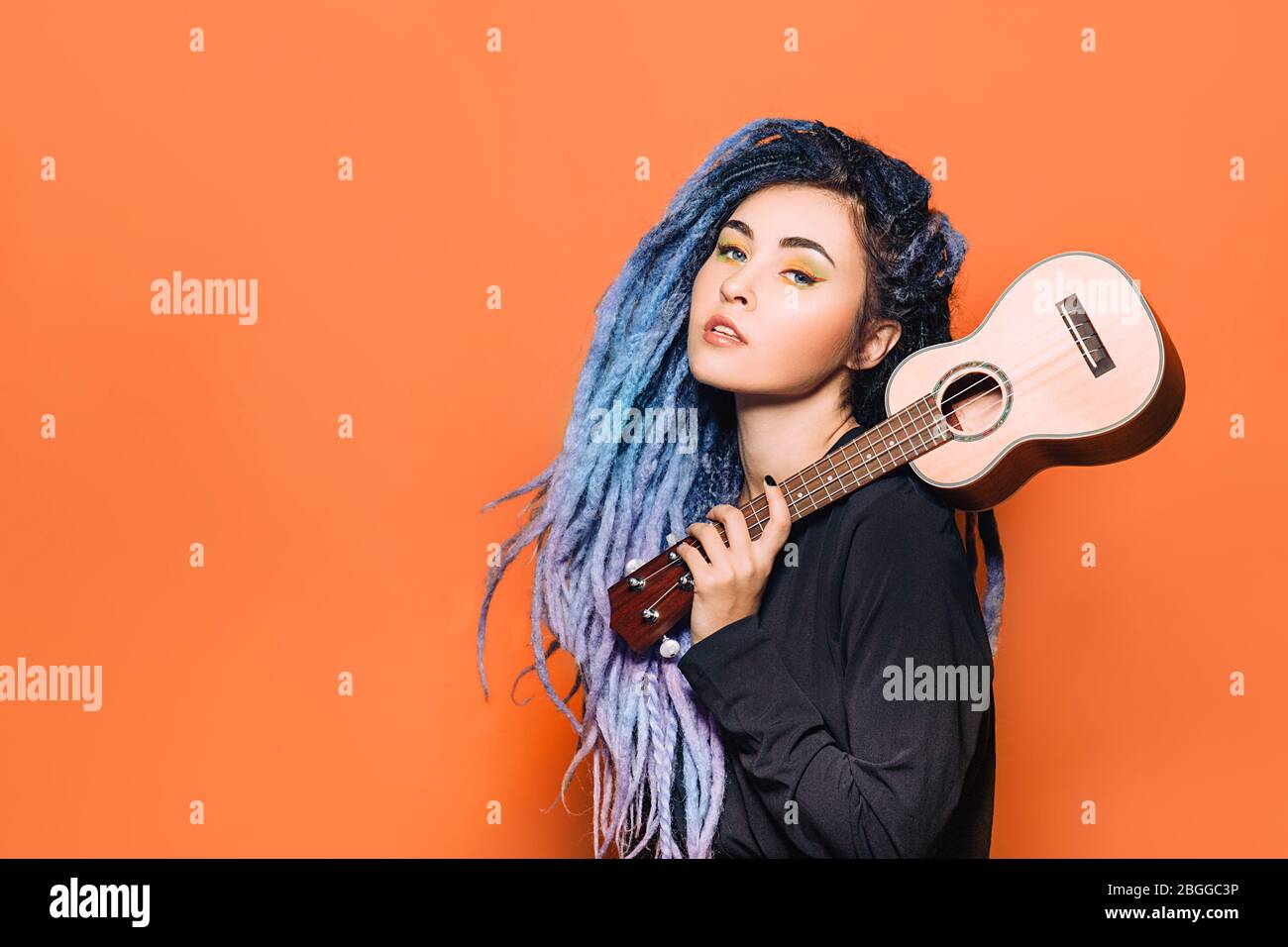 portrait of hipster woman with violet dreadlocks and ukulele in her hands on an orange background Stock Photo
