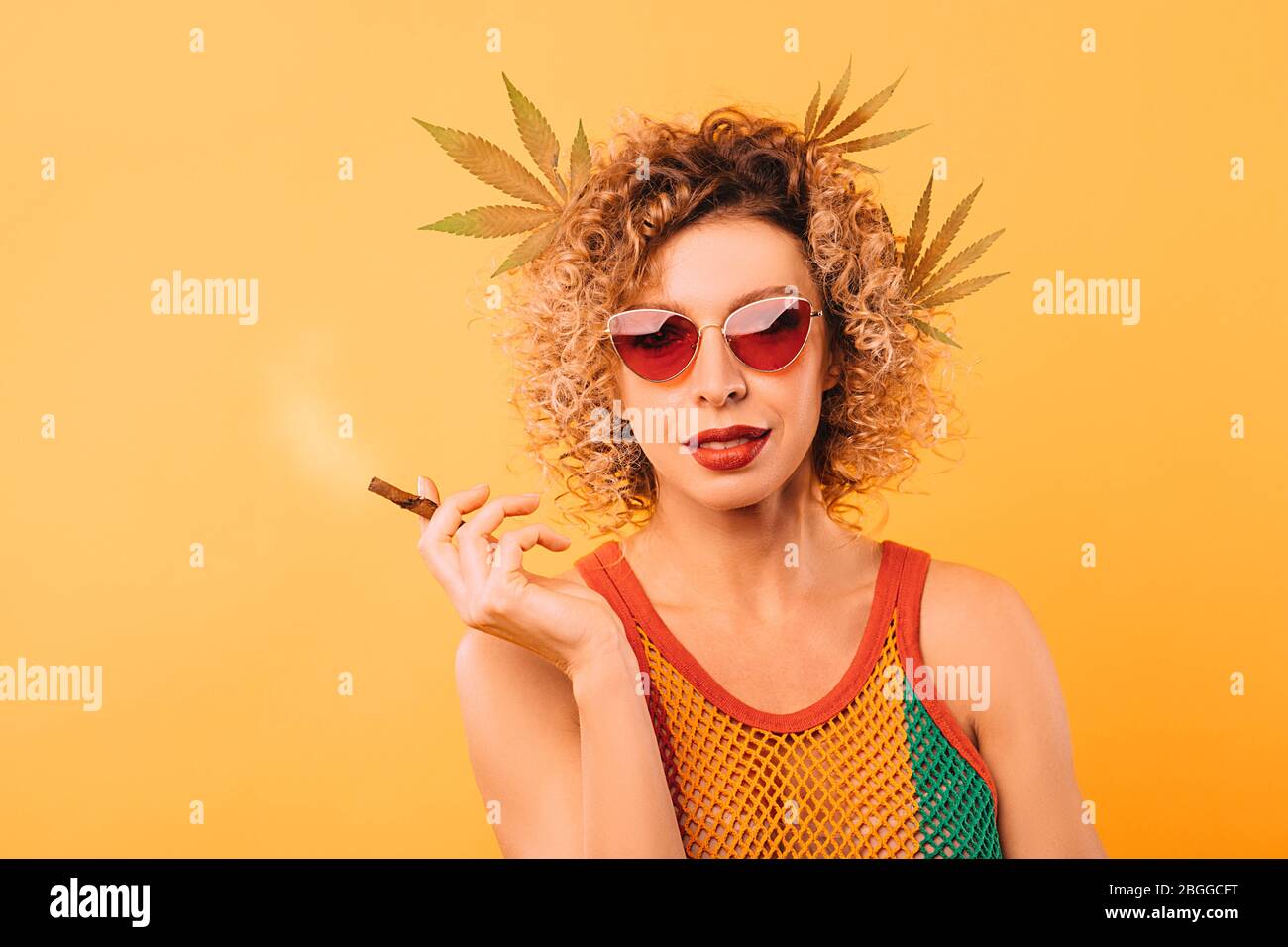 Hipster woman smokes a pipe with cannabis. Portrait of a woman with marijuana leaves in her hair Stock Photo