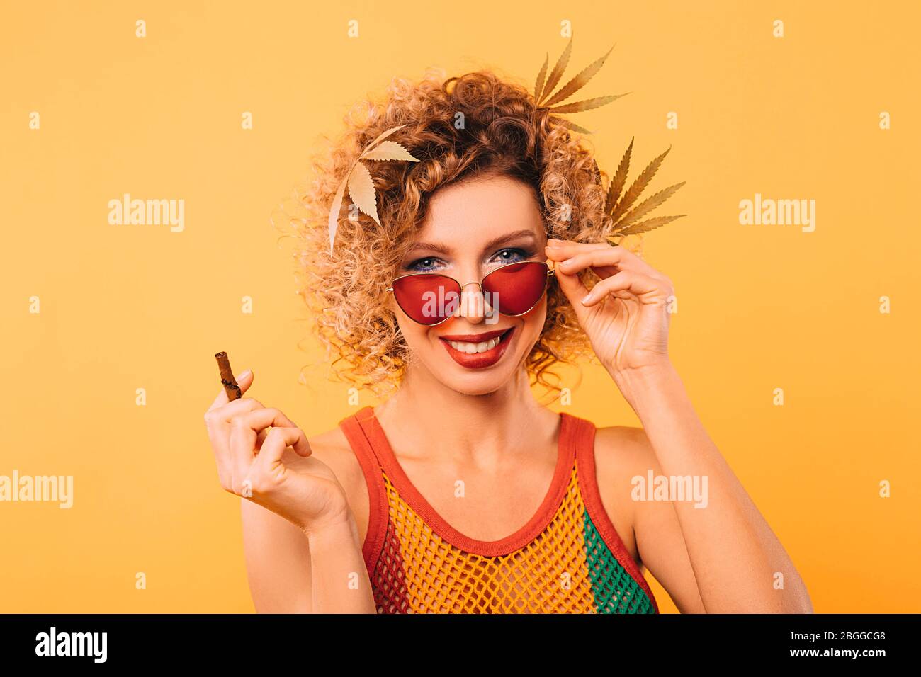 Rastafarian woman with marijuana leaves with her hair and stylish glasses holds a pipe for smoking cannabis Stock Photo