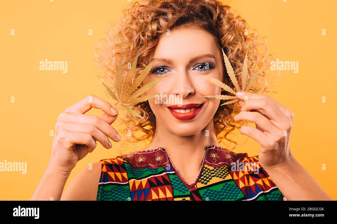 woman with a curly hairstyle and a smile on her face holds marijuana leaves in her hands. Legalization of cannabis Stock Photo