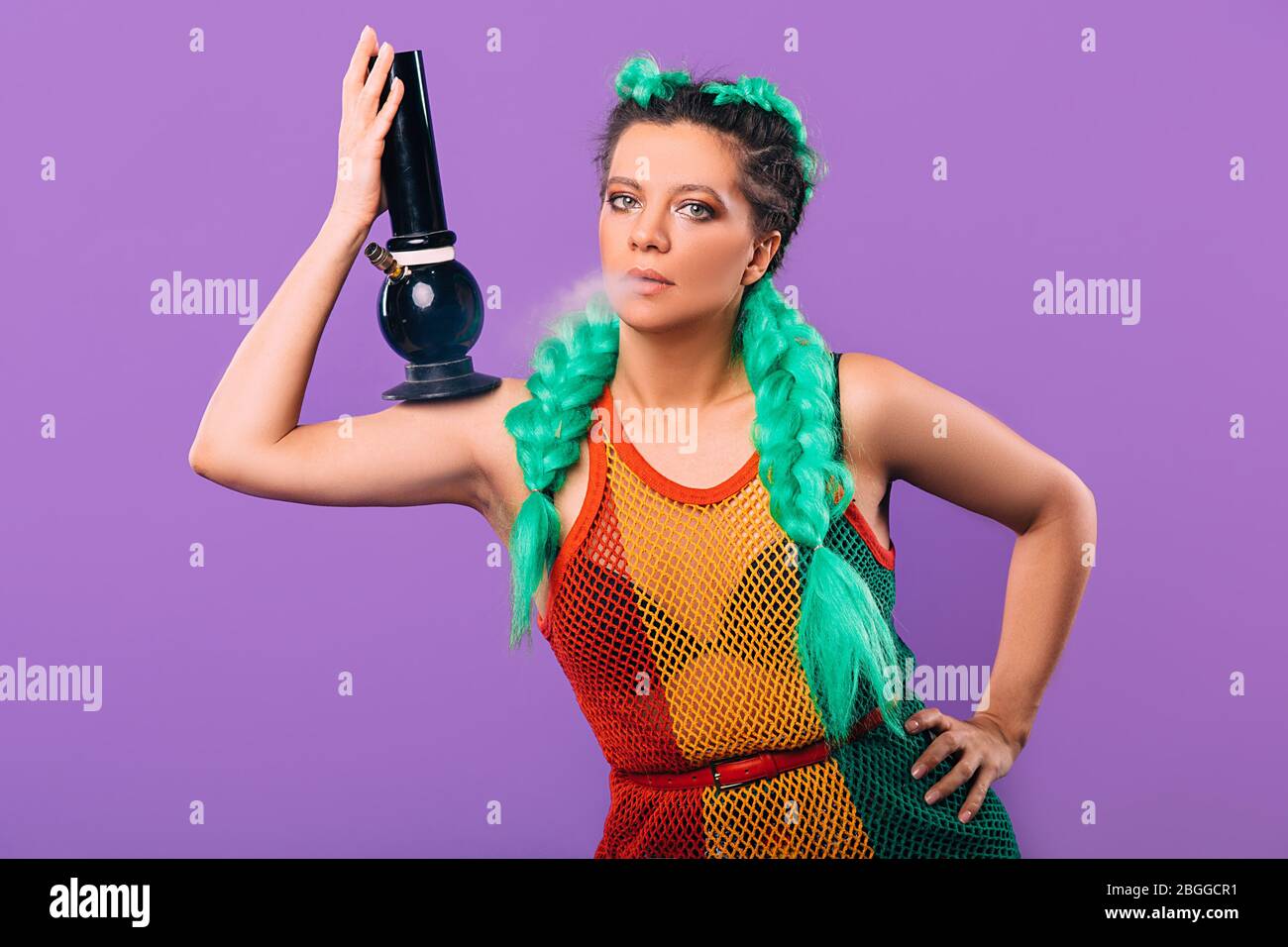 Rasta woman holds a bong in her hand. Legalization of marijuana. Cannabis smoking Bong on violet background Stock Photo