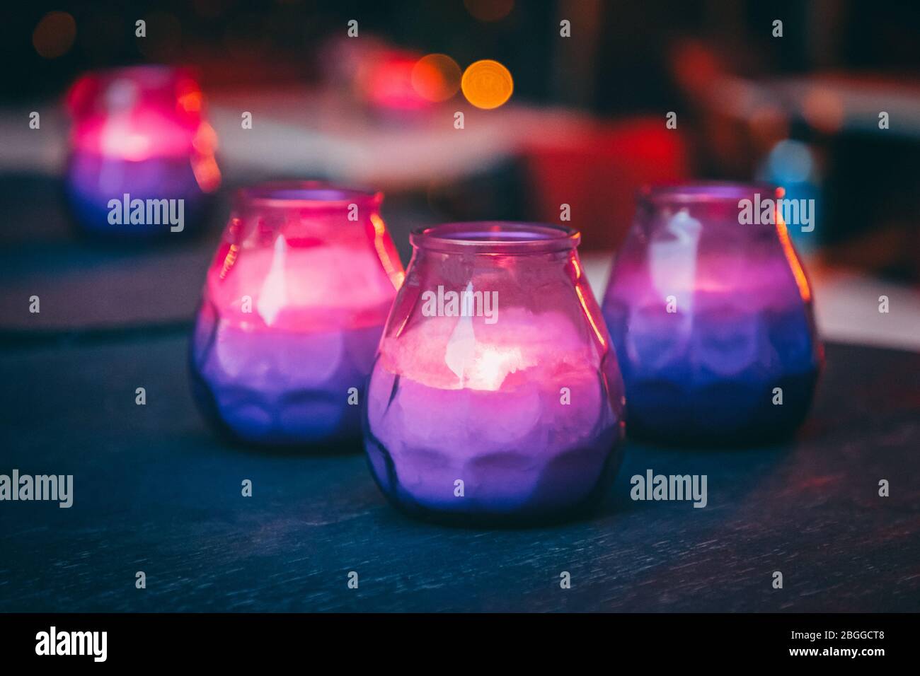 Hygge concept. Bright burning purple and pink candles on the dark table