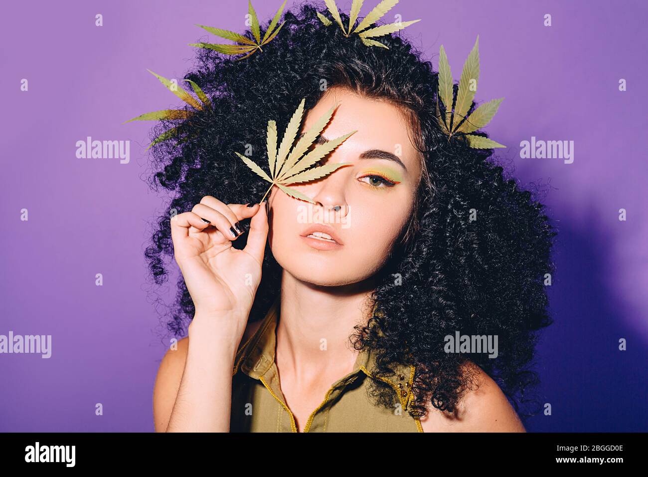 Portrait rastafarian woman with cannabis leaf near face. Legalization of marijuana. Close-up face on violet background Stock Photo