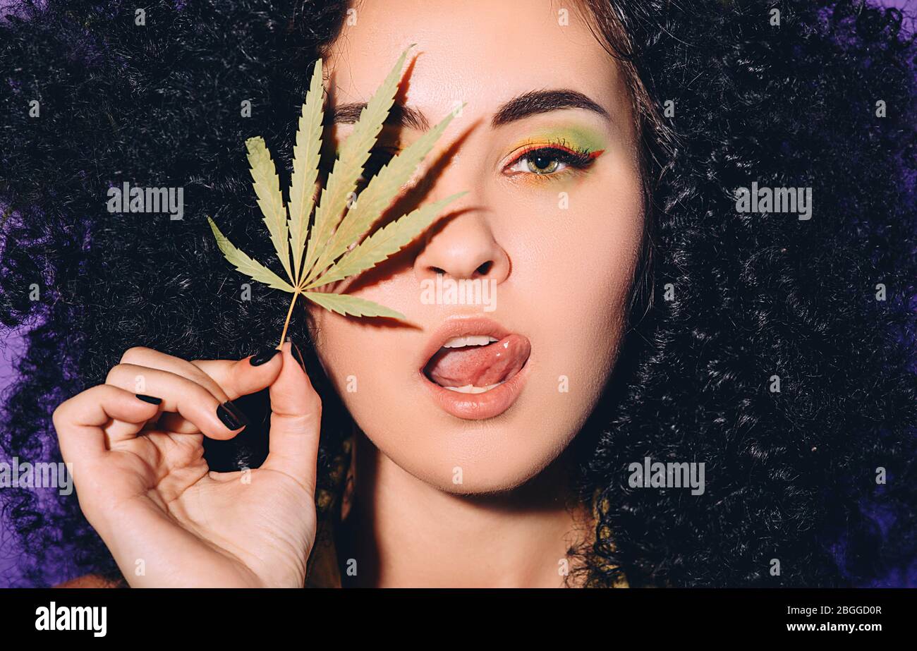 Portrait rastafarian woman with cannabis leaf near face. Legalization of marijuana. Close-up face on purple background Stock Photo
