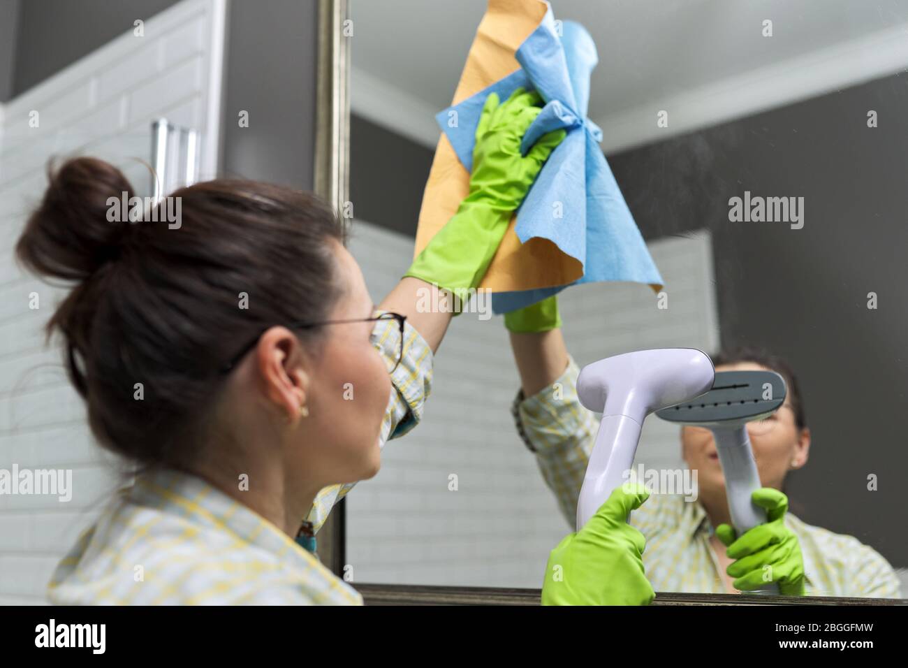 Woman doing cleaning in bathroom using vacuum cleaner, without use of household chemicals. Close-up of gloved hands with steam in the mirror, eco-frie Stock Photo