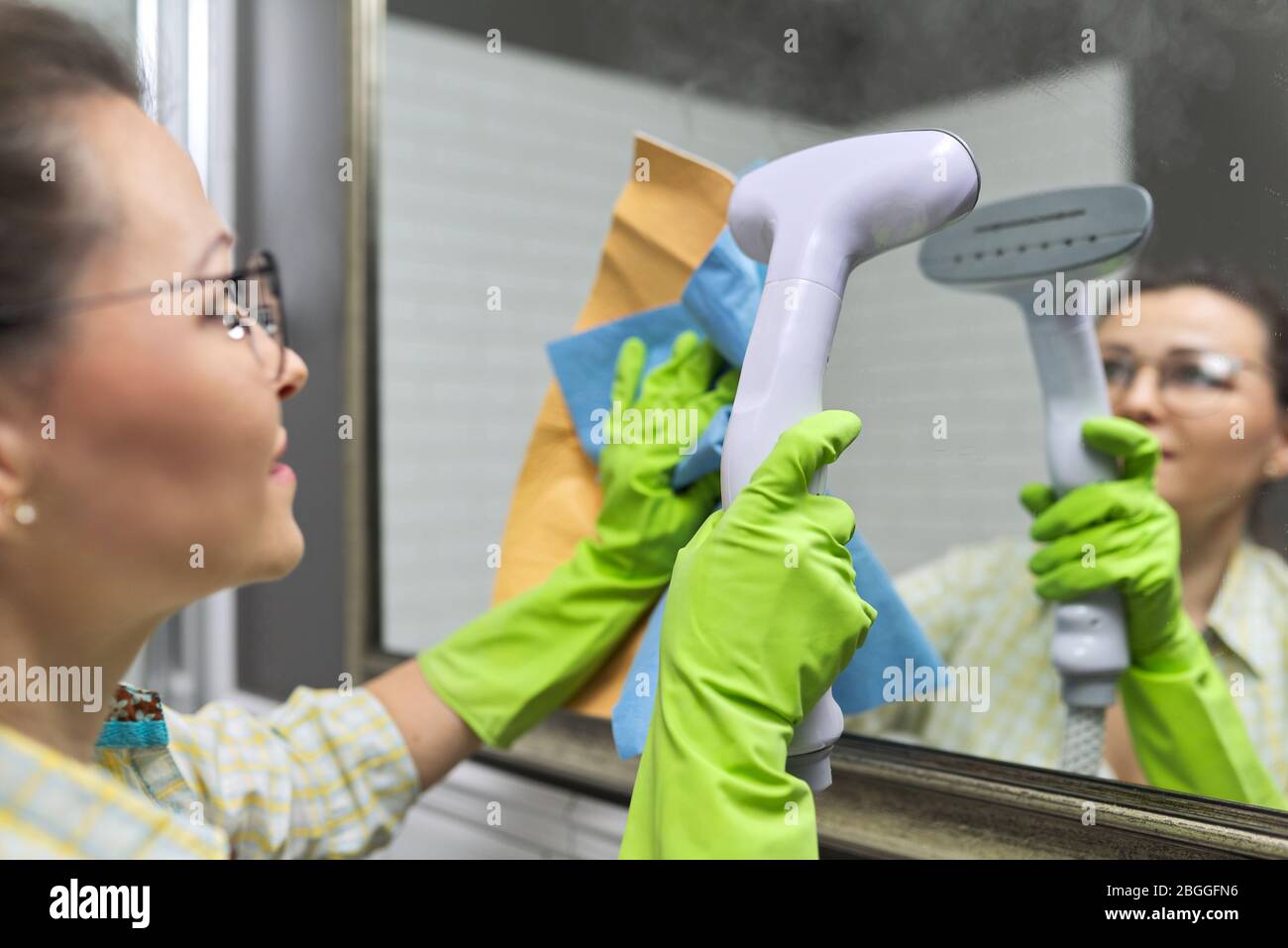 Woman doing cleaning in bathroom using vacuum cleaner, without use of household chemicals. Close-up of gloved hands with steam in the mirror, eco-frie Stock Photo