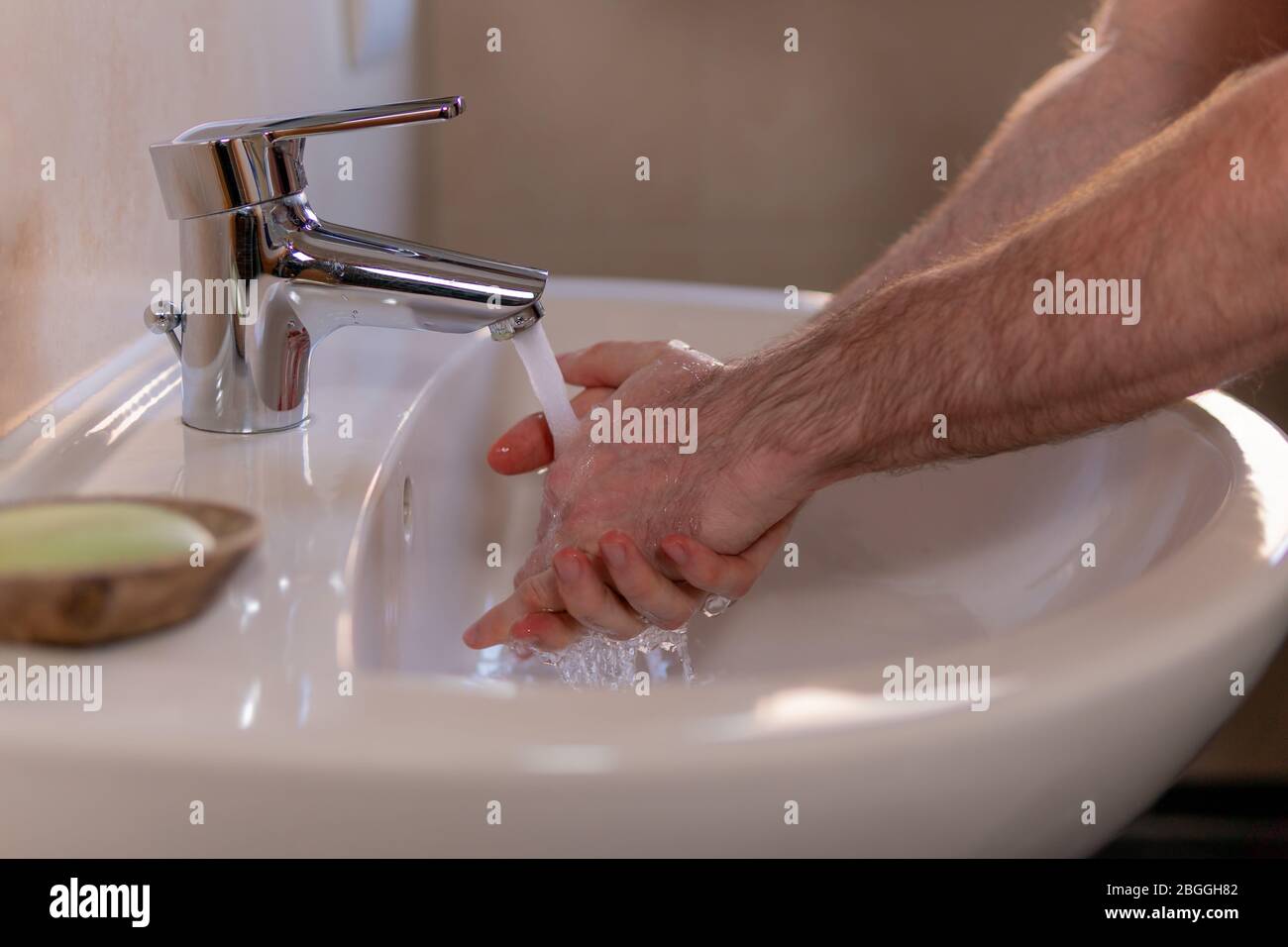 Caucasian man thoroughly washing hands in wash basin under water tap. Personal hygiene as coronavirus COVID-19 pandemic spread prevention. Stock Photo