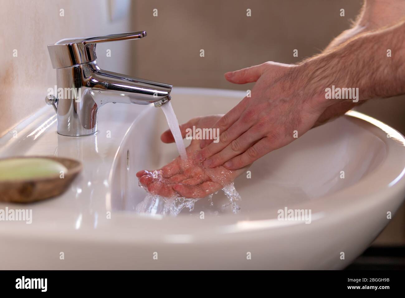 Caucasian man thoroughly washing hands in wash basin under water tap. Personal hygiene as coronavirus COVID-19 pandemic spread prevention. Stock Photo