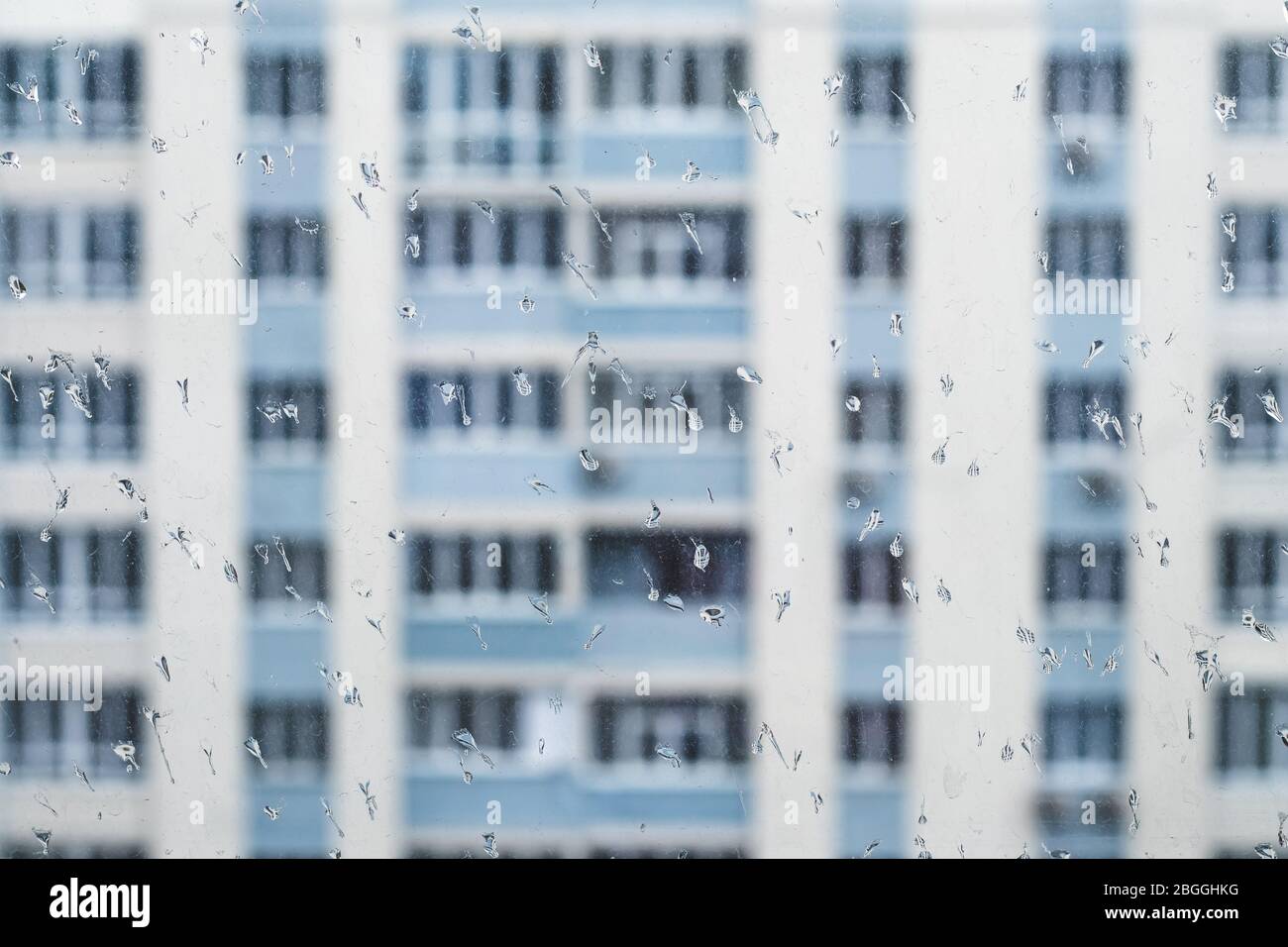 Dirty rainy window overlooking residential buildings, water drops on a glass. Self isolation concept, loneliness, sad mood Stock Photo