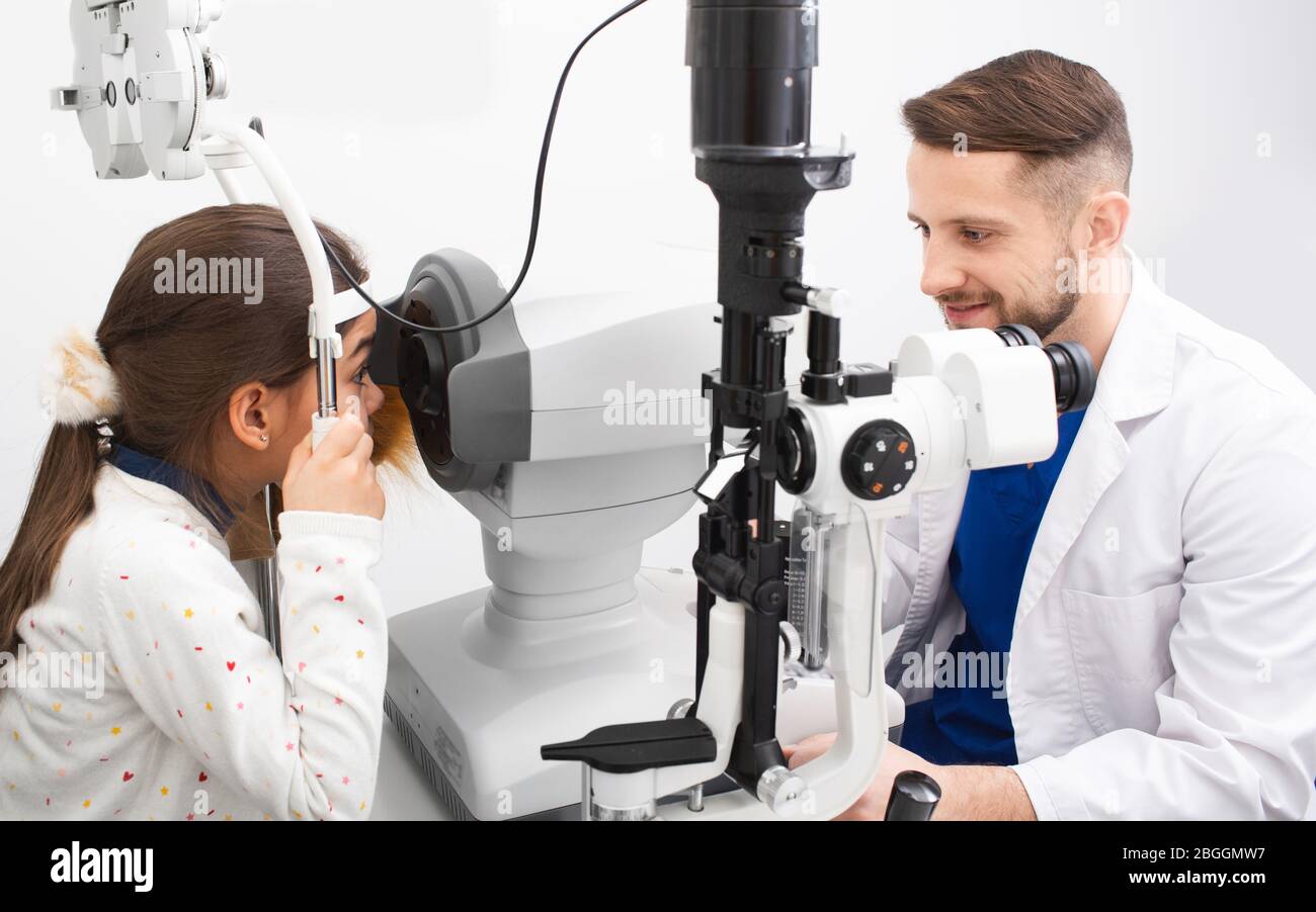 Male doctor looking very carefully at screen of ophthalmic tonometer to correctly check the girl's vision. Vision correction Stock Photo