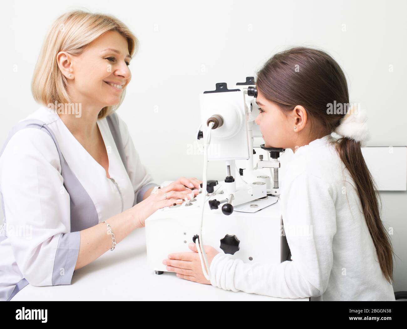 Mixed race girl is being examined at ophthalmic clinic. Female doctor using synoptophore doing eye diagnosis. Strabismus treatment Stock Photo
