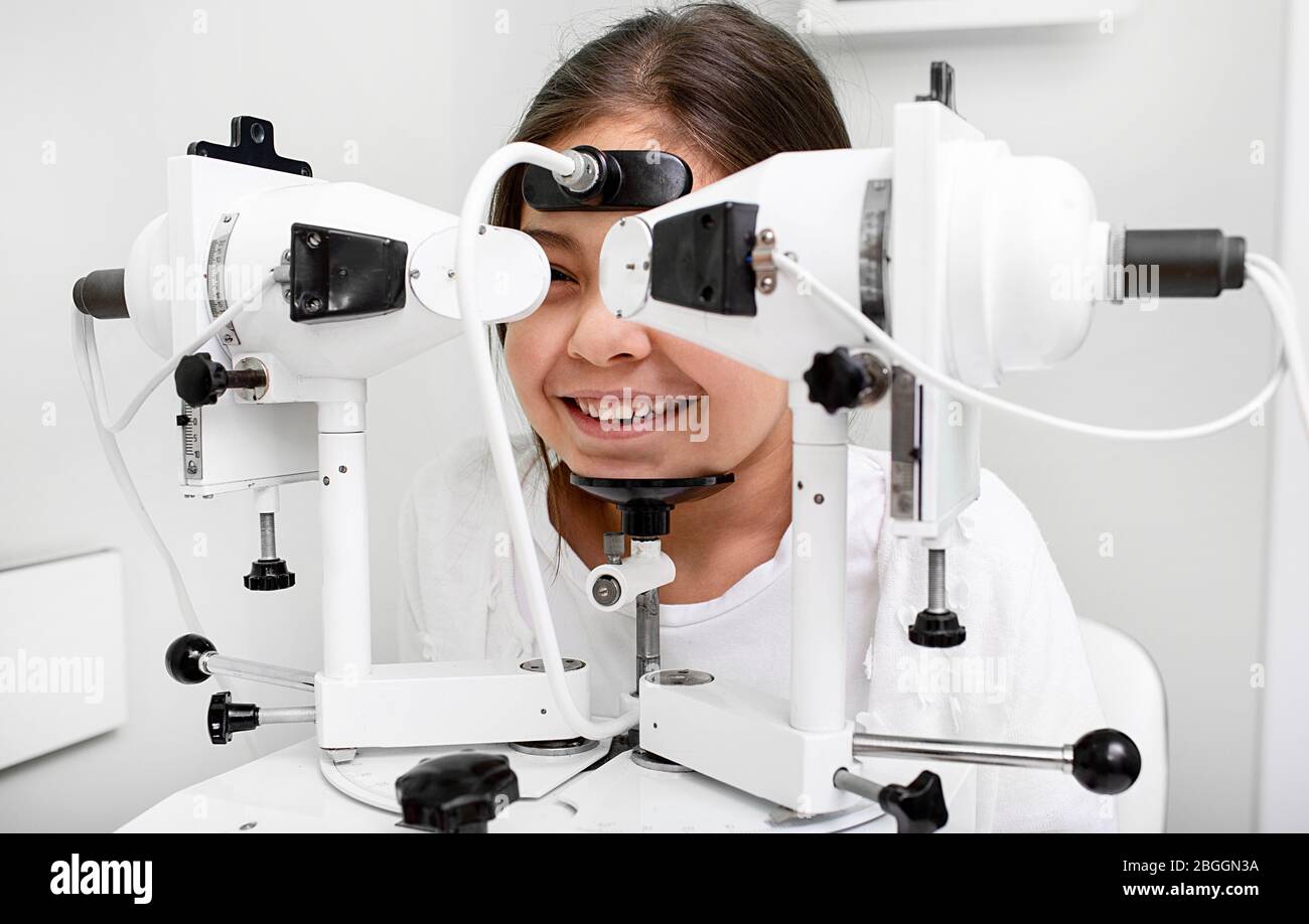 Mixed race girl near synoptophore to check her eyes. Diagnosis and treatment of strabismus in a vision clinic Stock Photo