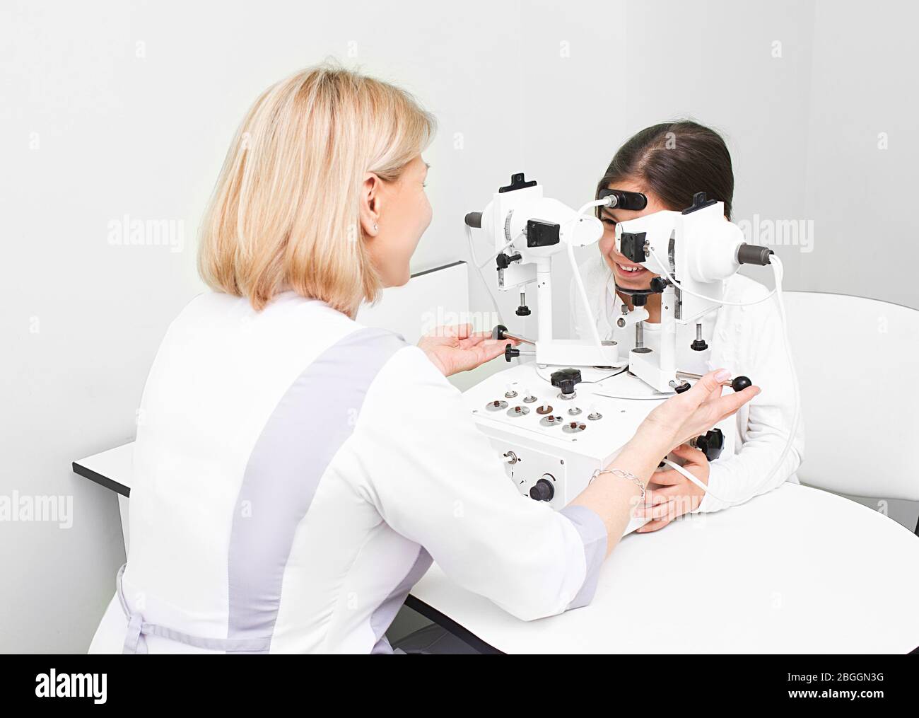 Feale doctor checking eyesight of a girl on modern equipment in clinic. Diagnosis and treatment of strabismus Stock Photo