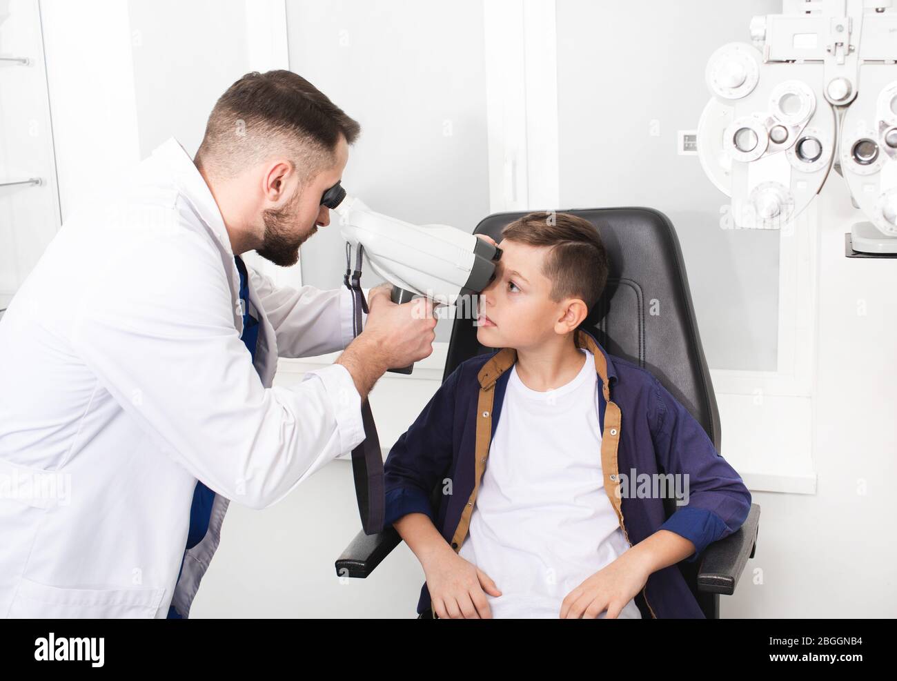 Male optometrist doing eye examination of boy patient. Manual tonometer for measuring intraocular pressure Stock Photo