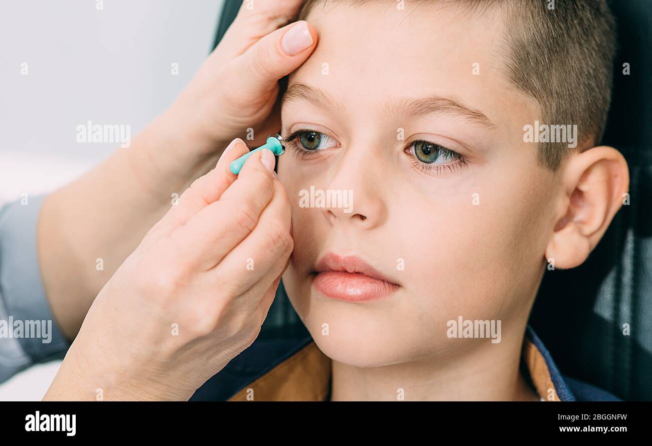 Optometrist trying on a contact lens to a teenage boy. Contact lenses for vision correction in