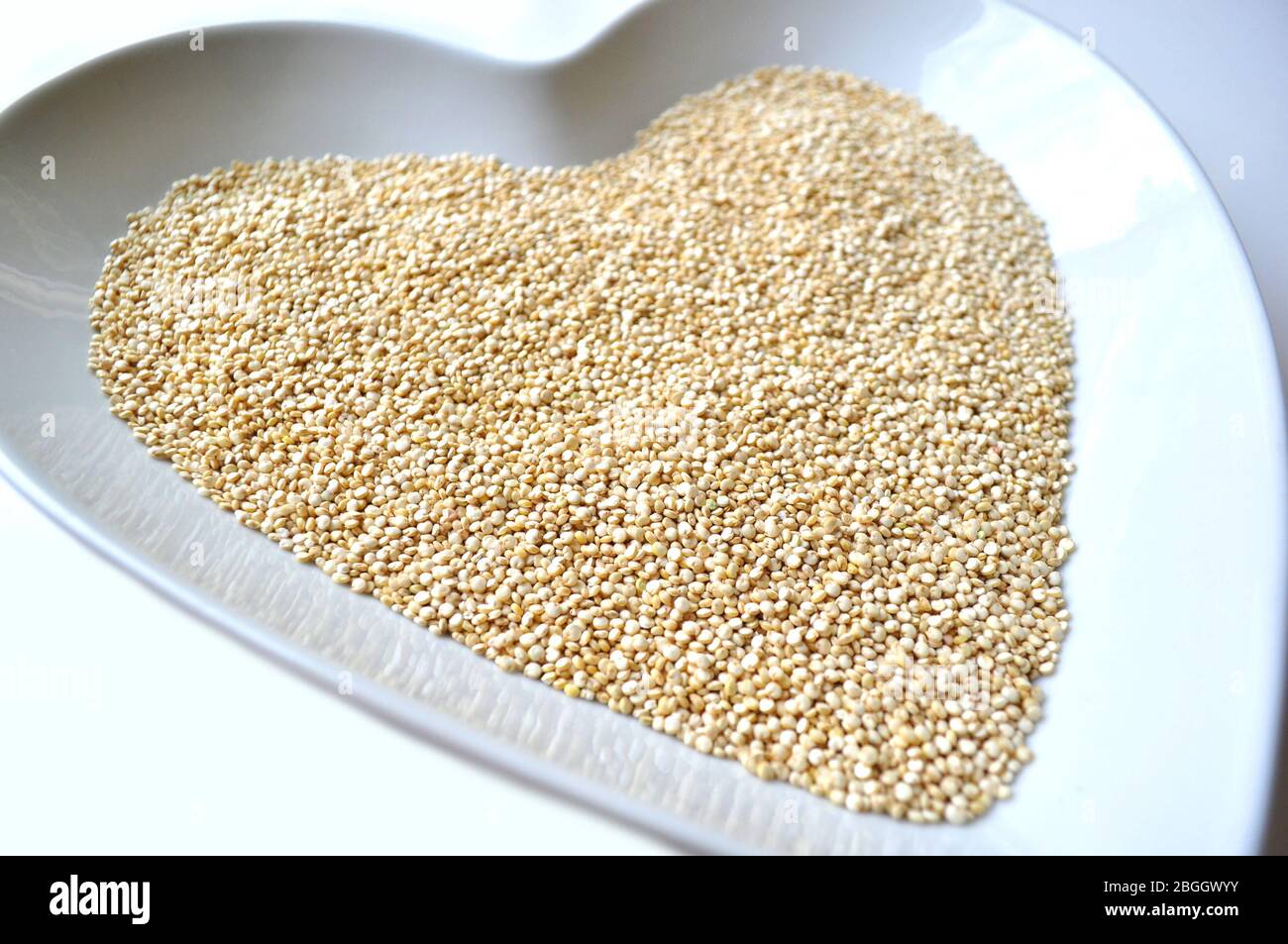 Organic gluten free quinoa grain in a heart shaped bowl on white with copy space Stock Photo