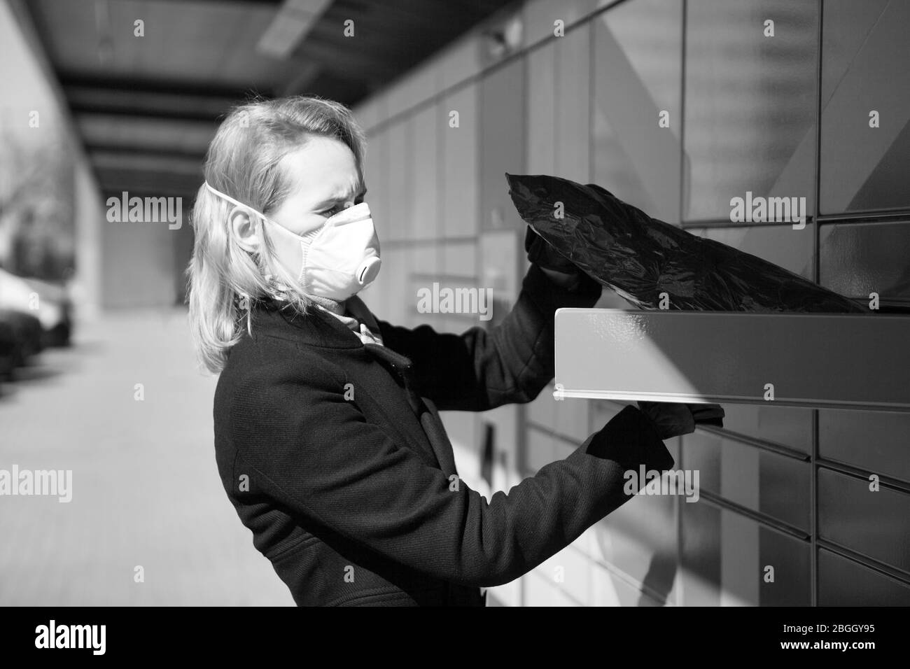 lady wearing a face mask receives a parcel or package from a post parcel terminal in Tallinn. woman wearing a face respiratory mask -protecting from Stock Photo