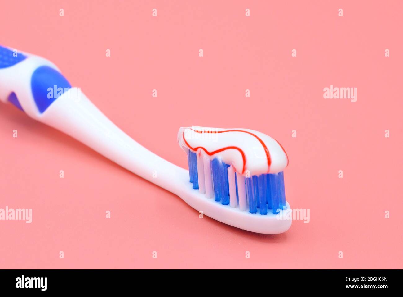 White toothbrush with red swirl of toothpaste on pink background