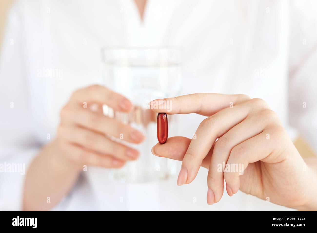 Healthcare and medical concept. Close-up view of woman holding pill in one hand and glass of water in the another hand. Focus on the pill. Coronavirus Stock Photo