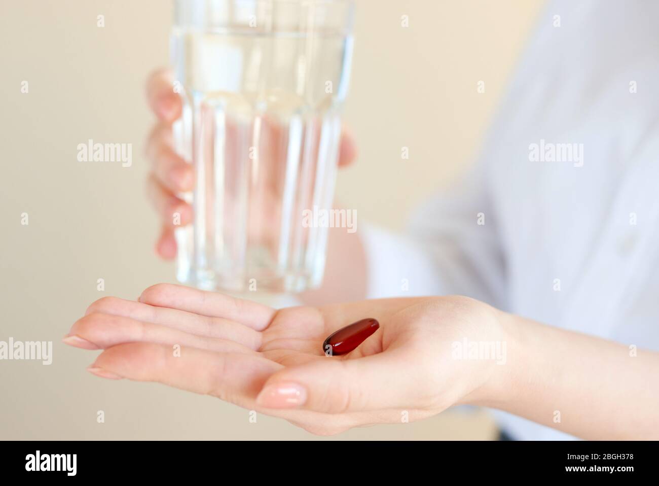 Healthcare and medical concept. Close-up view of woman holding pill in one hand and glass of water in the another hand. Focus on the pill. Coronavirus Stock Photo