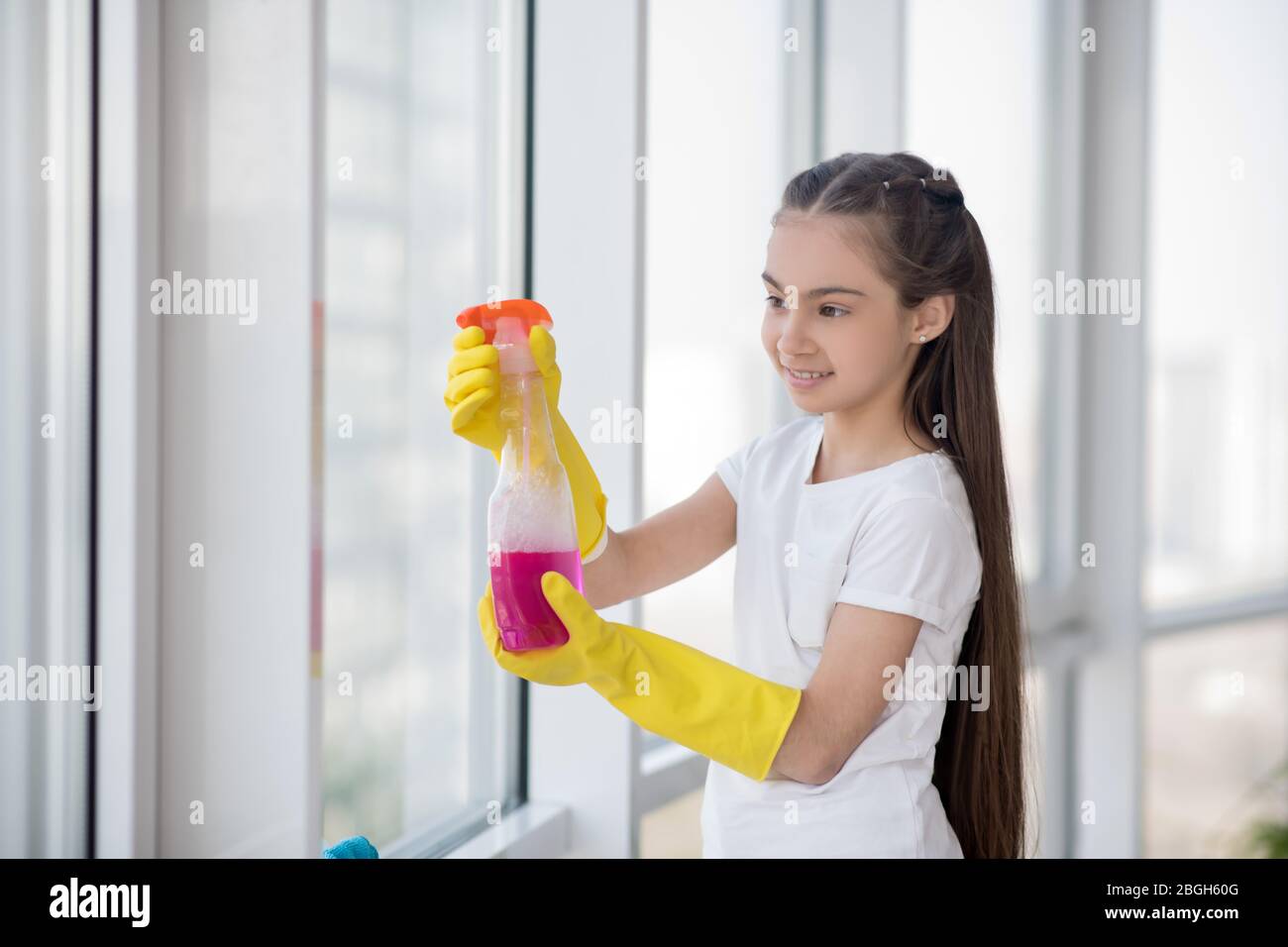 Long-haired teenage girl in rudiments washing a window. Stock Photo