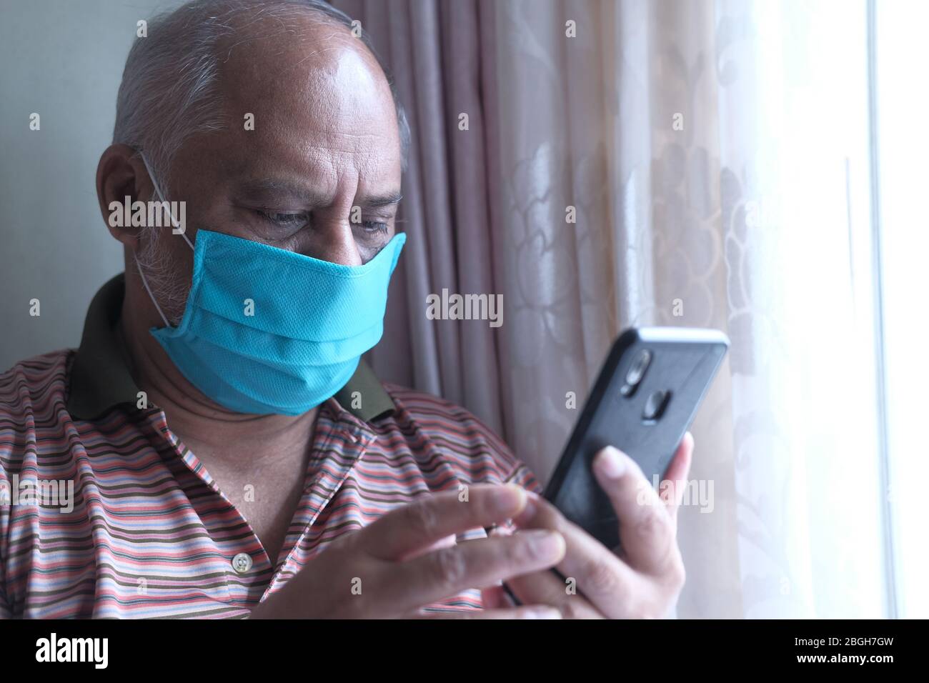 senior man with mask using smart phone indoor  Stock Photo