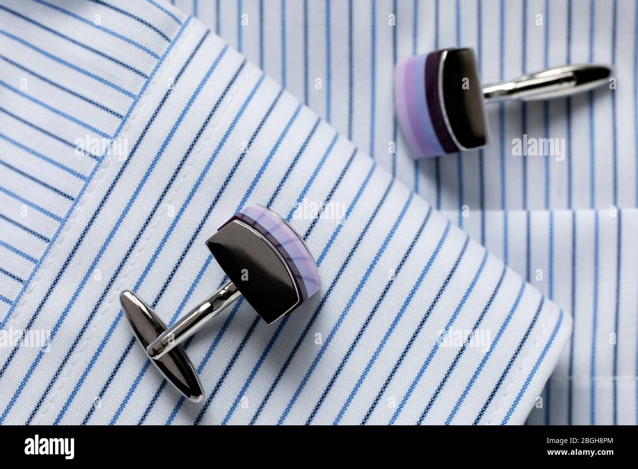 Striped white and blue men's shirt with multicolored cufflinks. Business dress code. Close-up. Selecrive focus. Stock Photo