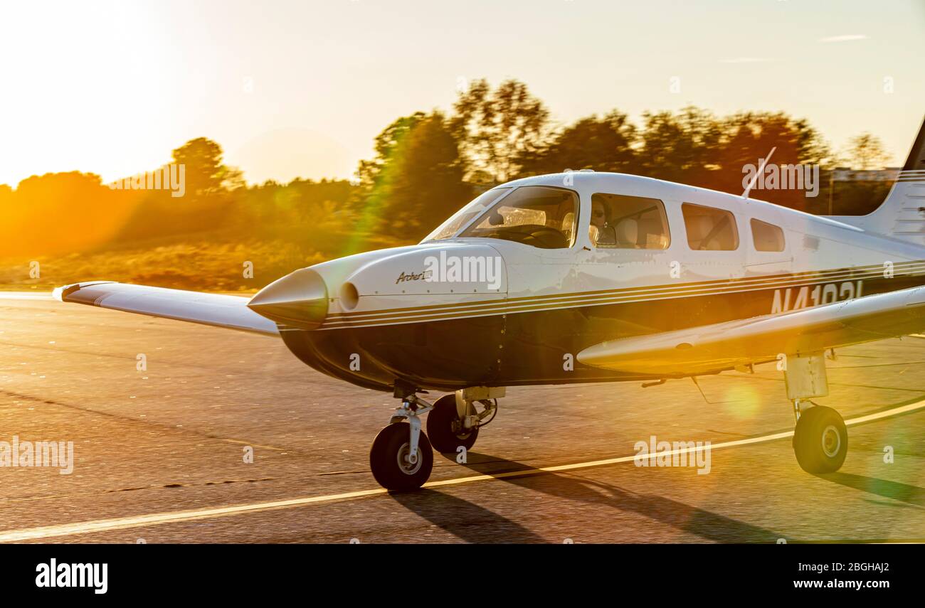 A Piper Archer III general aviation aircraft taxis by in the late afternoon sun. Stock Photo