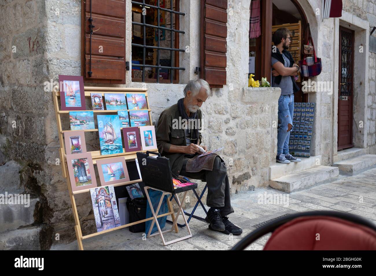 Montenegro, Sep 17, 2018: An artist sits next to his paintings displayed on the street of Kotor Old Town Stock Photo