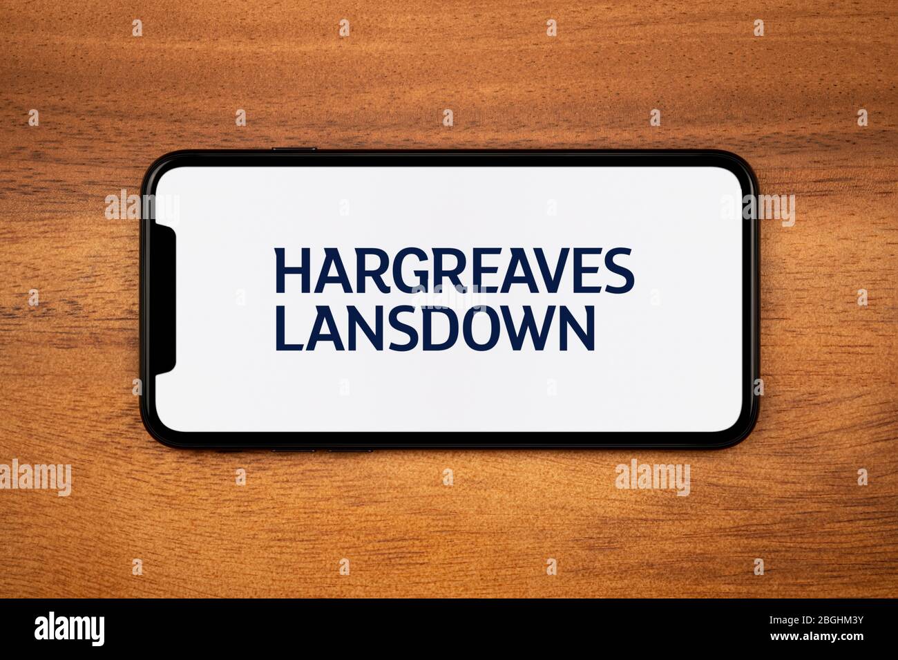 A smartphone showing the Hargreaves Lansdown logo rests on a plain wooden table (Editorial use only). Stock Photo