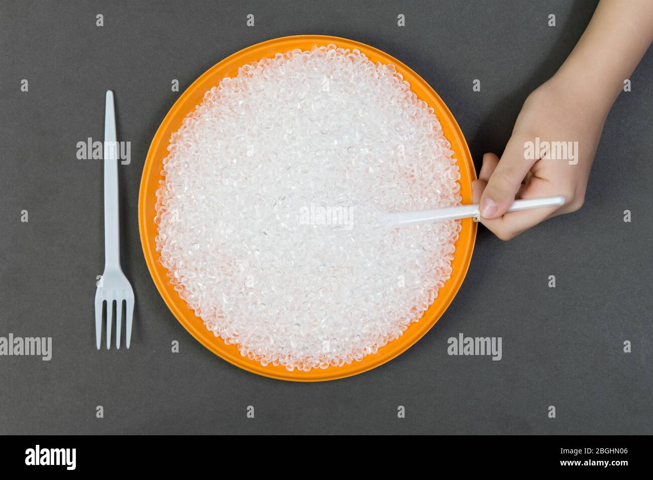 Plastic plate with recycled plastic pellets and fork with a spoon on a dark background, a person eats plastic pallets .Concept of environmental pollut Stock Photo