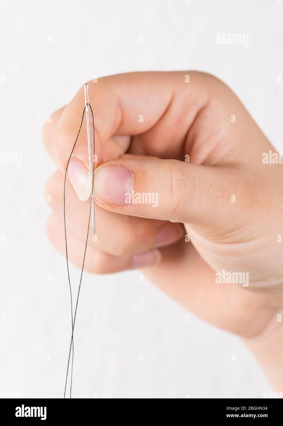 Detail of hand holding needle with thread on white background Stock