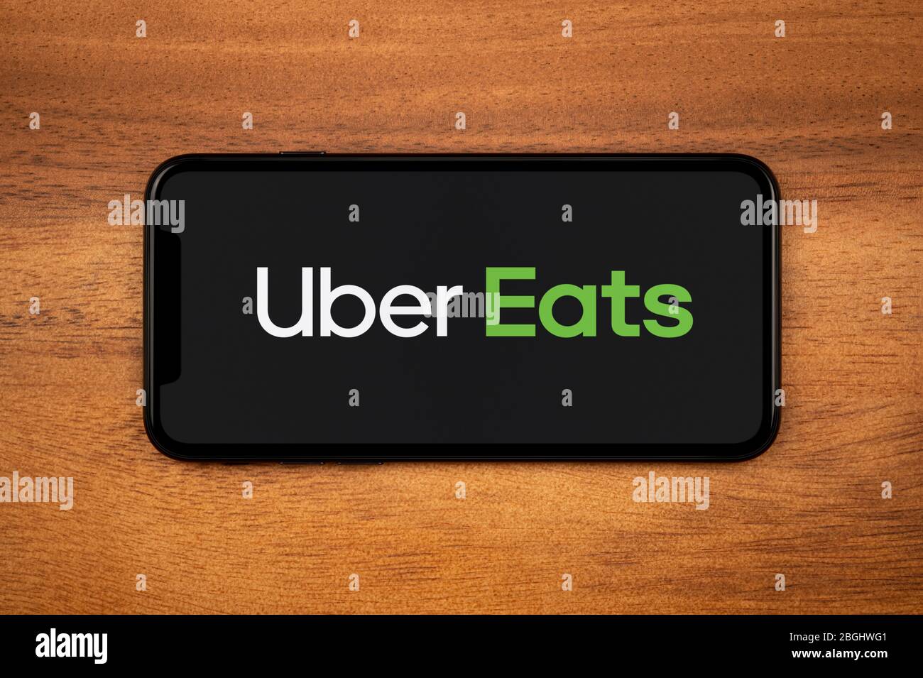 A smartphone showing the Uber Eats logo rests on a plain wooden table (Editorial use only). Stock Photo