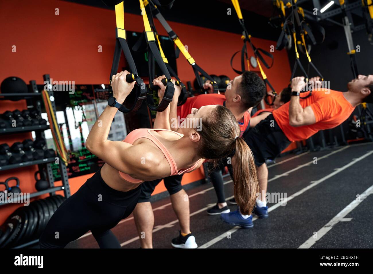 Sporty Lifestyle. Young people doing low row TRX exercise at gym back ...